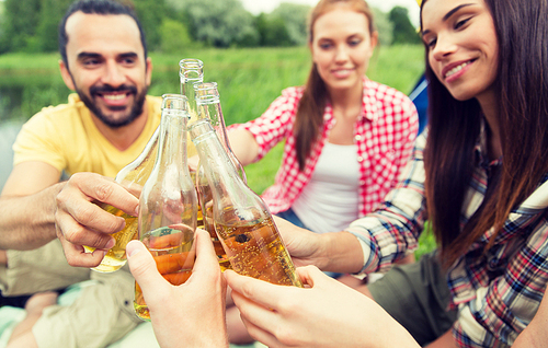 camping, travel, tourism, hike and people concept - happy friends clinking glass bottles and drinking cider or beer at campsite