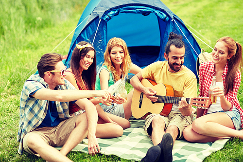 travel, tourism, hike, picnic and people concept - group of happy friends with tent and drinks playing guitar at camping