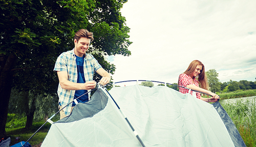 camping, travel, tourism, hike and people concept - happy couple setting up tent outdoors