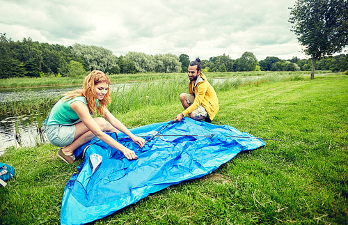 camping, travel, tourism, hike and people concept - happy couple setting up tent outdoors