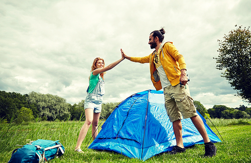 camping, travel, tourism, hike and people concept - happy couple setting up tent outdoors