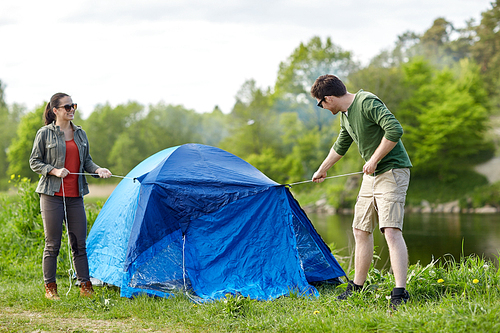 camping, travel, tourism, hike and people concept - happy couple setting up tent outdoors