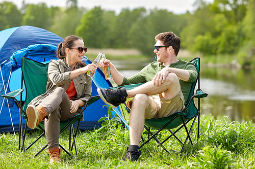 camping, travel, tourism, hike and people concept - happy couple clinking beer bottles at campsite tent