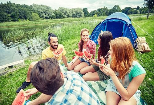 travel, tourism, hike, picnic and people concept - group of happy friends with tent eating watermelon at camping