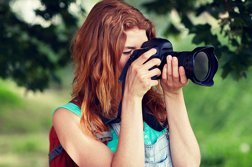 travel, tourism, hike, hobby and people concept - young woman with backpack and camera photographing outdoors