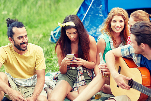 travel, tourism, hike, picnic and people concept - group of happy friends with smartphone and drinks playing guitar at camping