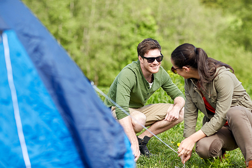 camping, travel, tourism, hike and people concept - happy couple setting up tent outdoors