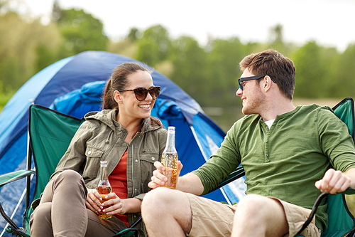 camping, travel, tourism, hike and people concept - happy couple drinking beer or cider at campsite tent