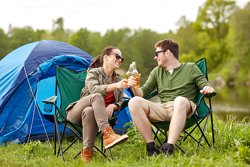 camping, travel, tourism, hike and people concept - happy couple clinking beer bottles at campsite tent