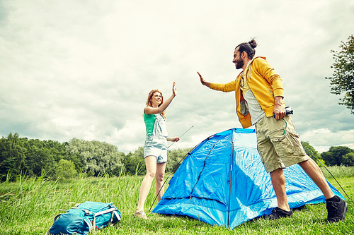 camping, travel, tourism, hike and people concept - happy couple setting up tent outdoors