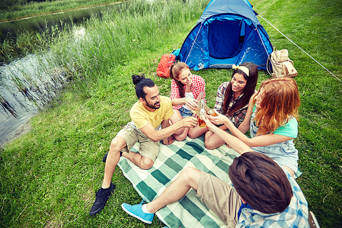 camping, travel, tourism, hike and people concept - happy friends with glass bottles drinking cider or beer at campsite