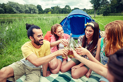 camping, travel, tourism, hike and people concept - happy friends with glass bottles drinking cider or beer at campsite