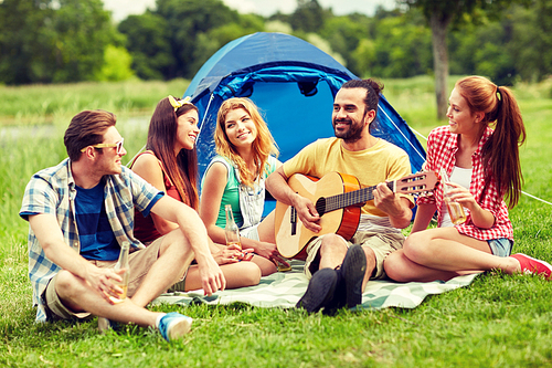 travel, tourism, hike, picnic and people concept - group of happy friends with tent and drinks playing guitar at camping