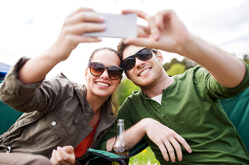 travel, hiking, technology, tourism and people concept - smiling couple of travelers taking selfie by smartphone at camping