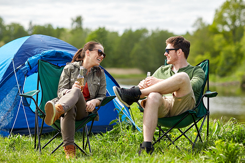 camping, travel, tourism, hike and people concept - happy couple drinking beer or cider at campsite tent