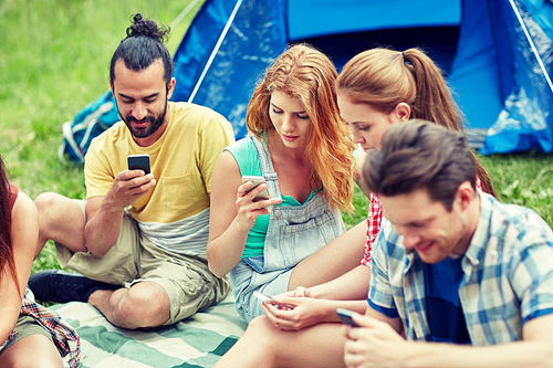 travel, tourism, hike, technology and people concept - group of friends with smartphone and tent at camping