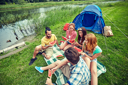 travel, tourism, hike, picnic and people concept - group of happy friends with tent eating watermelon at camping