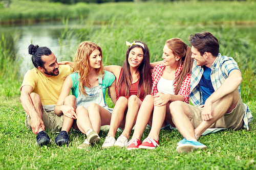 friendship, leisure, summer and people concept - group of smiling friends sitting on grass and talking outdoors