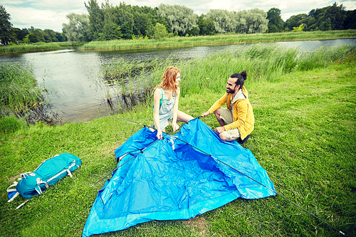 camping, travel, tourism, hike and people concept - happy couple setting up tent outdoors