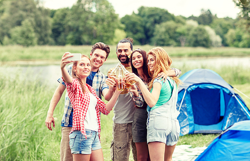 camping, travel, tourism, hike and people concept - happy friends with glass bottles drinking cider or beer and taking selfie by smartphone at camping