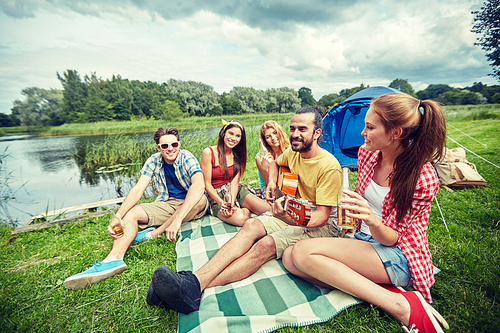 travel, tourism, hike, picnic and people concept - group of happy friends with tent and drinks playing guitar at camping