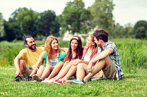 friendship, leisure, summer and people concept - group of smiling friends sitting on grass and talking outdoors