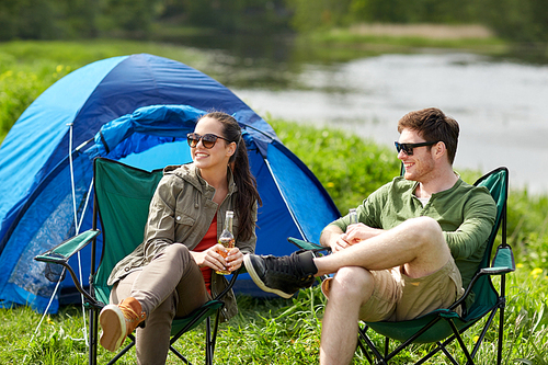 camping, travel, tourism, hike and people concept - happy couple drinking beer or cider at campsite tent