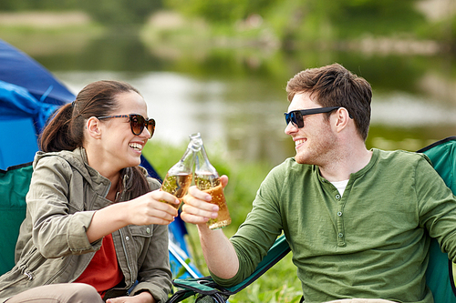 camping, travel, tourism, hike and people concept - happy couple clinking beer bottles at campsite tent