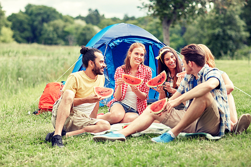 travel, tourism, hike, picnic and people concept - group of happy friends with tent eating watermelon at camping