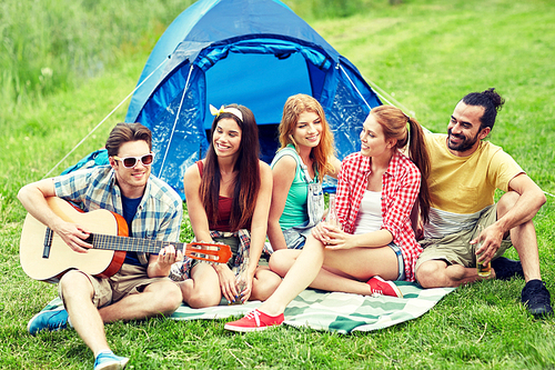 travel, tourism, hike, picnic and people concept - group of happy friends with tent and drinks playing guitar at camping