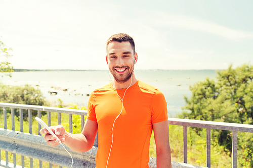 fitness, sport, people, technology and healthy lifestyle concept - smiling young man with smartphone and earphones listening to music at summer seaside