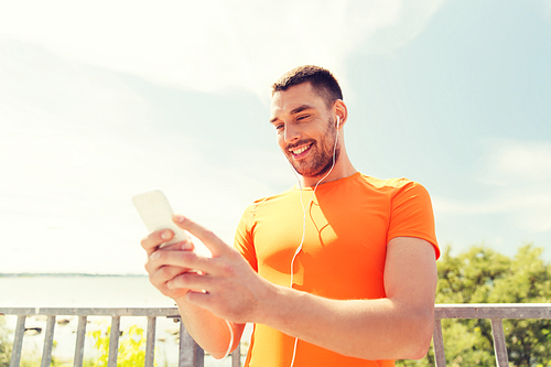 fitness, sport, people, technology and healthy lifestyle concept - smiling young man with smartphone and earphones listening to music at summer seaside