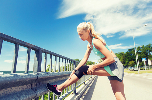 fitness, sport, exercising and healthy lifestyle concept - young woman with injured knee or leg outdoors