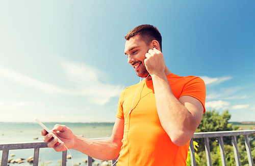 fitness, sport, people, technology and healthy lifestyle concept - smiling young man with smartphone and earphones listening to music at summer seaside