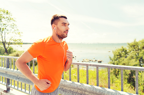 fitness, sport, people, technology and healthy lifestyle concept - happy man with earphones running outdoors