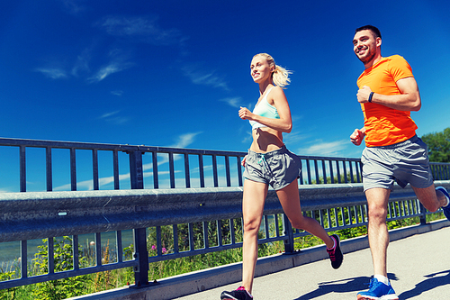 fitness, sport, friendship and healthy lifestyle concept - smiling couple with heart-rate watch running at summer seaside