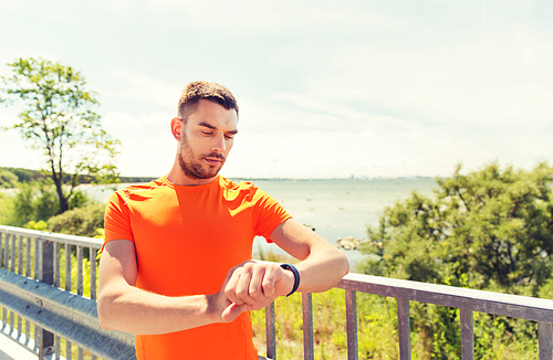 fitness, sport, people and healthy lifestyle concept - young man with smart wristwatch at summer seaside