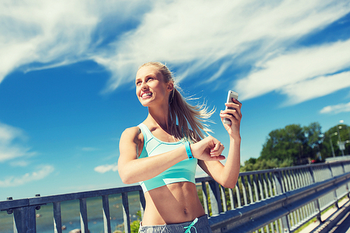 fitness, sport, people, technology and healthy lifestyle concept - smiling young woman with heart rate watch and smartphone exercising outdoors