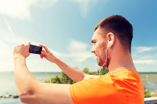 fitness, sport, people, technology and healthy lifestyle concept - smiling young man with smartphone and earphones listening to music at summer seaside