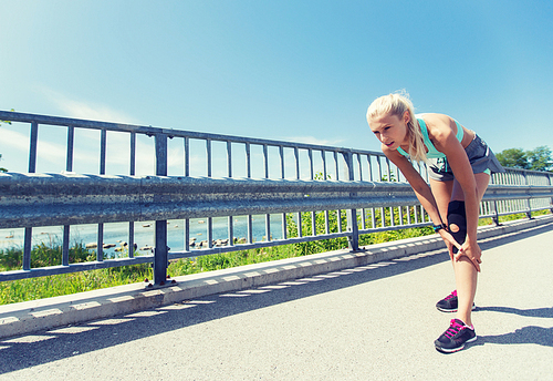 fitness, sport, exercising and healthy lifestyle concept - young woman with knee support brace injured leg outdoors