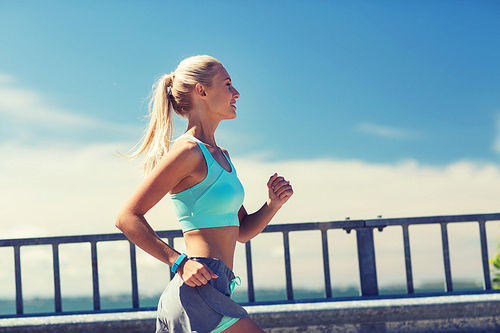 fitness, sport, people and healthy lifestyle concept - smiling young woman with heart rate watch running outdoors