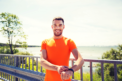 fitness, sport, people, technology and healthy lifestyle concept - smiling young man with smart wristwatch at summer seaside