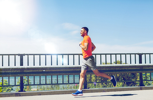 fitness, sport, people, technology and healthy lifestyle concept - smiling young man with heart rate watch running at summer seaside