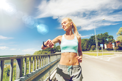 fitness, sport, people, technology and healthy lifestyle concept - smiling young woman with heart rate watch running outdoors