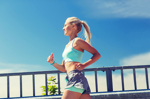 fitness, sport, people and healthy lifestyle concept - smiling young woman with heart rate watch running outdoors