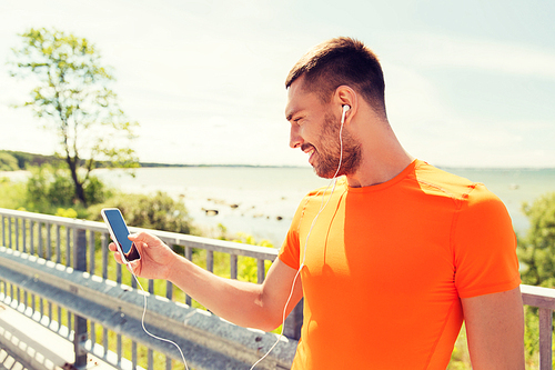 fitness, sport, people, technology and healthy lifestyle concept - smiling young man with smartphone and earphones listening to music at summer seaside