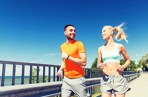 fitness, sport, friendship and healthy lifestyle concept - smiling couple with heart-rate watch running at summer seaside