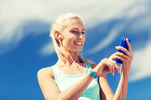 fitness, sport, people, technology and healthy lifestyle concept - smiling young woman with smartphone and earphones listening to music and exercising outdoors