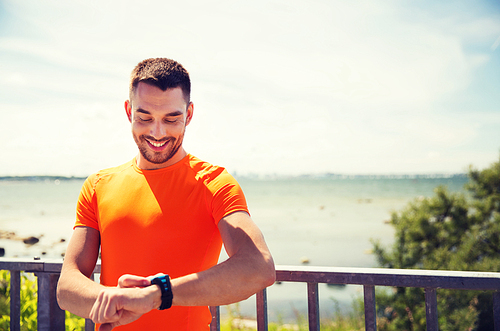 fitness, sport, people, technology and healthy lifestyle concept - smiling young man with smart wristwatch at summer seaside