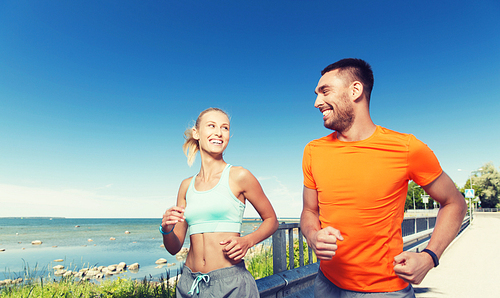 fitness, sport, friendship and healthy lifestyle concept - smiling couple running at summer seaside